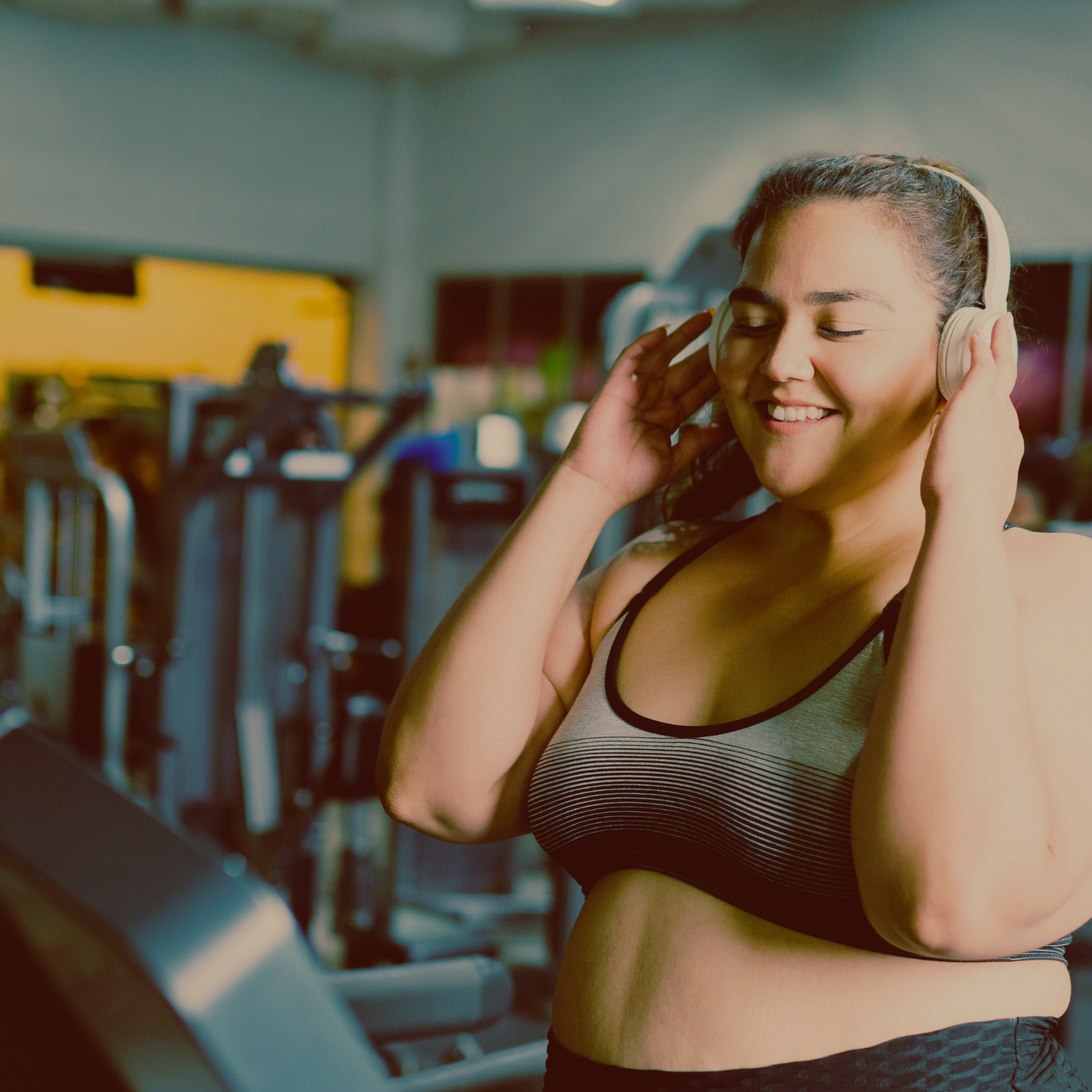 Woman enjoying music on her headphones while getting ready to run an a treadmill at the gym.